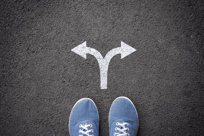 Behavioural Science Uncertain road sign with multiple directions on asphalt surface, person standing in front.
